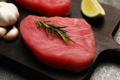 Photo of Raw tuna fillet with rosemary on dark wooden board, closeup