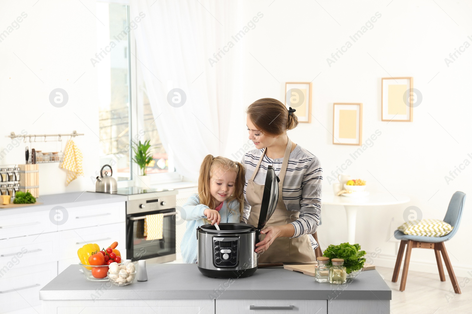 Photo of Mother and daughter preparing food with modern multi cooker in kitchen