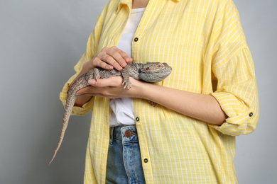 Photo of Woman holding bearded lizard on grey background, closeup. Exotic pet