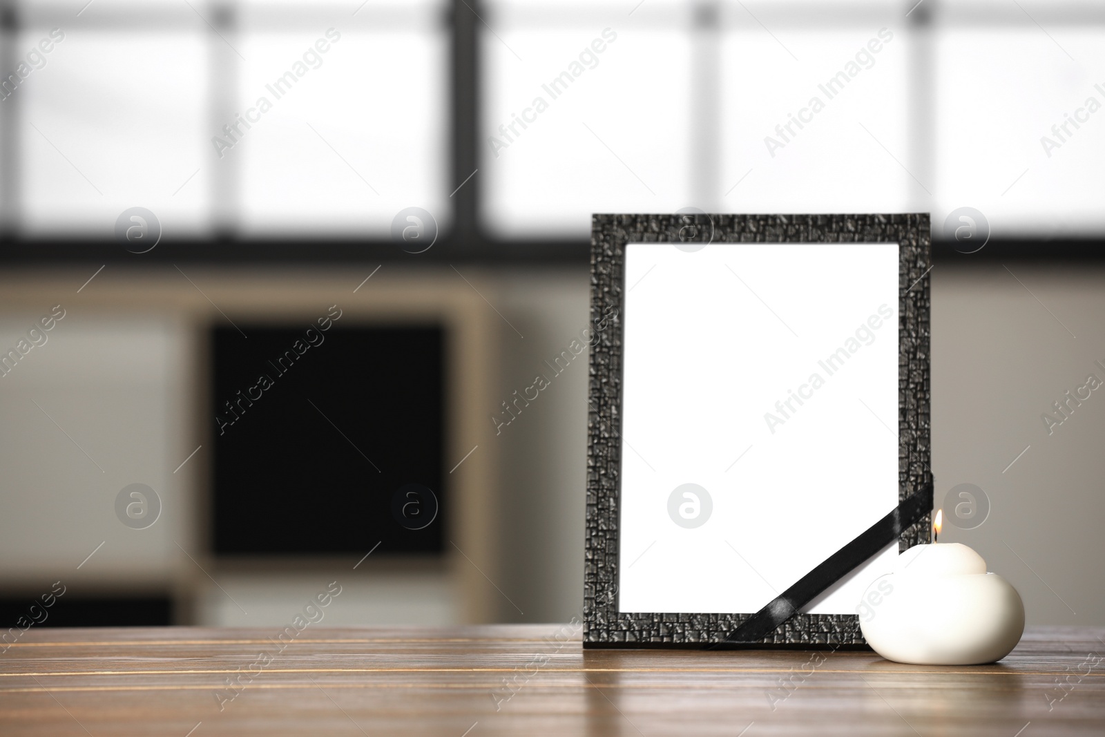 Photo of Funeral photo frame with black ribbon and candle on wooden table indoors. Space for design