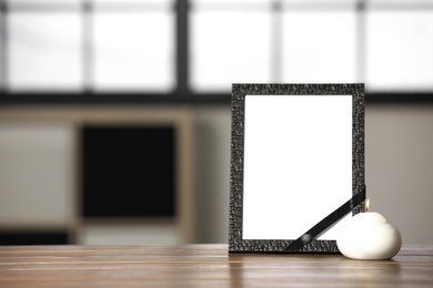 Photo of Funeral photo frame with black ribbon and candle on wooden table indoors. Space for design