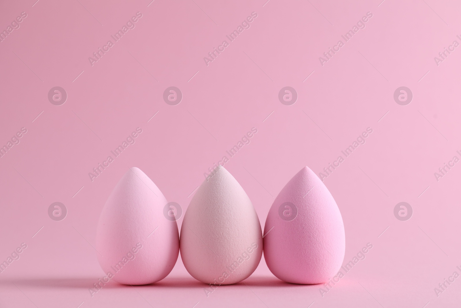 Photo of Three colorful makeup sponges on pink background. Space for text