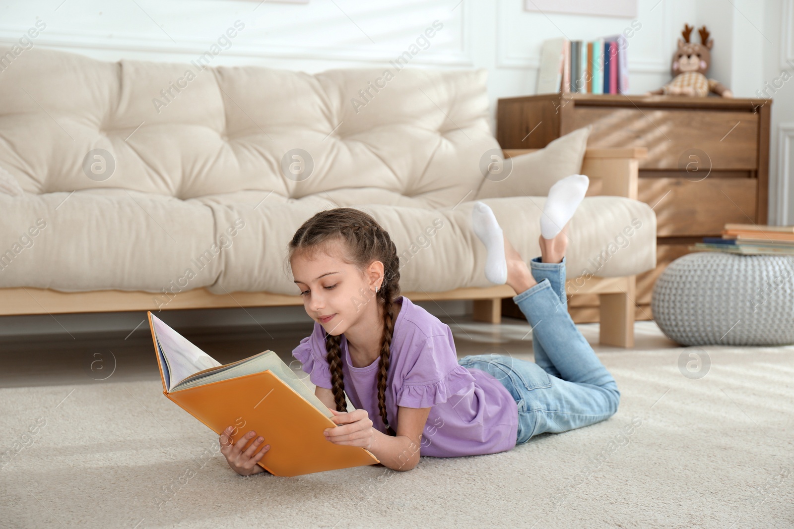 Photo of Cute little girl reading book on floor at home