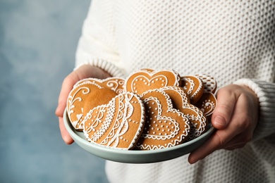 Photo of Woman holding plate with heart shaped gingerbread cookies on blue background, closeup