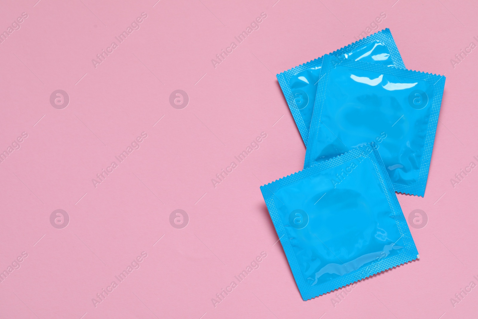 Photo of Condom packages on pink background, flat lay and space for text. Safe sex