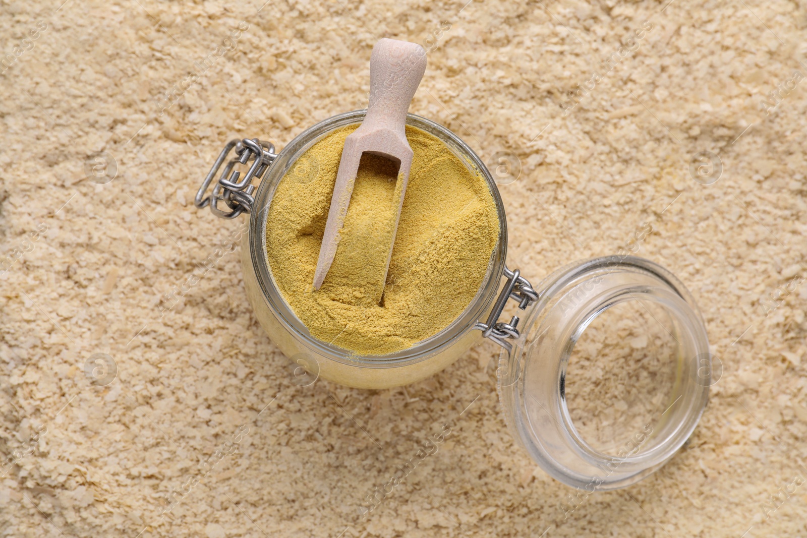 Photo of Glass jar and wooden scoop of granulated brewer`s yeast on flakes, top view