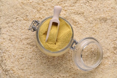 Photo of Glass jar and wooden scoop of granulated brewer`s yeast on flakes, top view