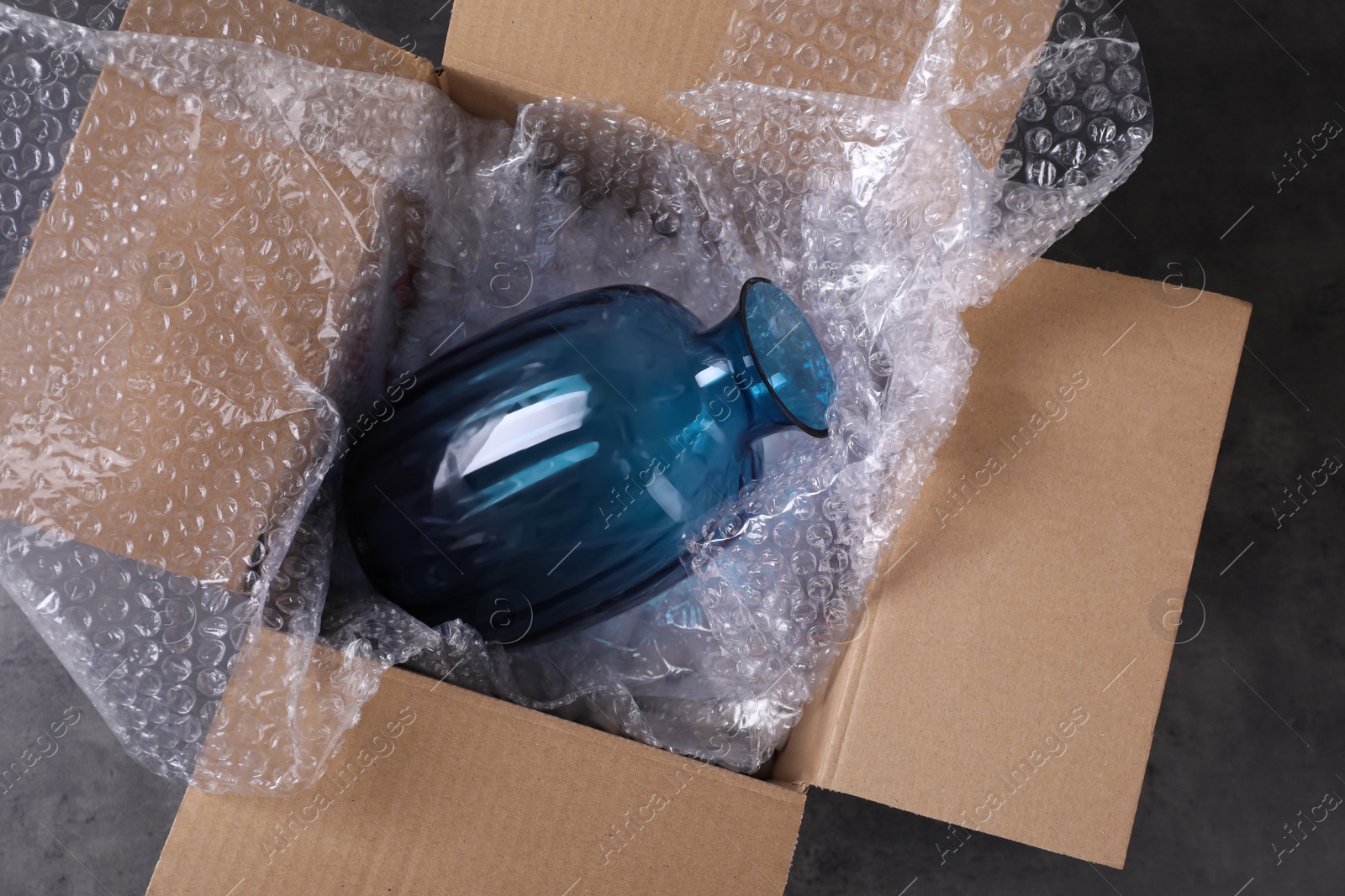 Photo of Beautiful glass vase in box with bubble wrap on dark grey table, top view