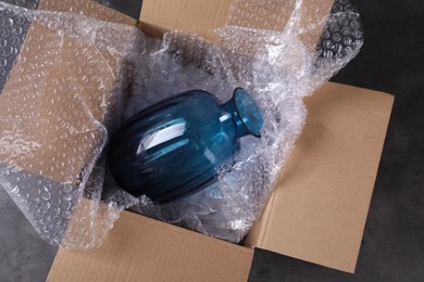 Photo of Beautiful glass vase in box with bubble wrap on dark grey table, top view