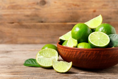 Tasty ripe limes in bowl on wooden table, closeup. Space for text