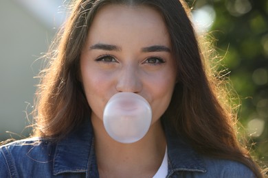 Photo of Beautiful young woman blowing bubble gum outdoors