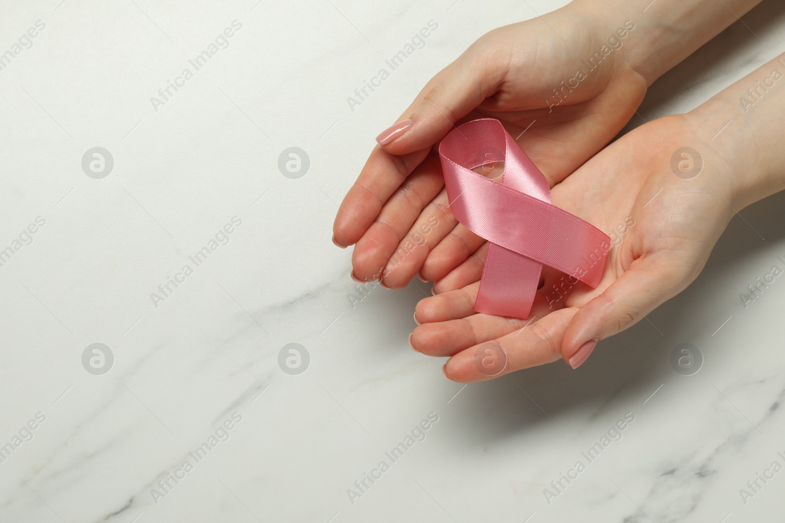 Photo of Breast cancer awareness. Woman with pink ribbon at white marble table, top view. Space for text