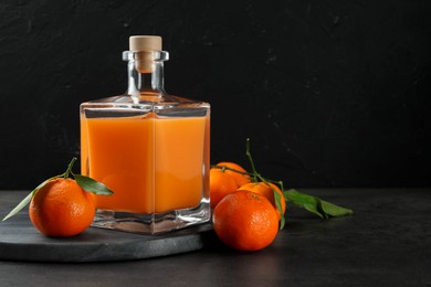 Photo of Delicious tangerine liqueur in glass bottle and fresh fruits on grey table, space for text