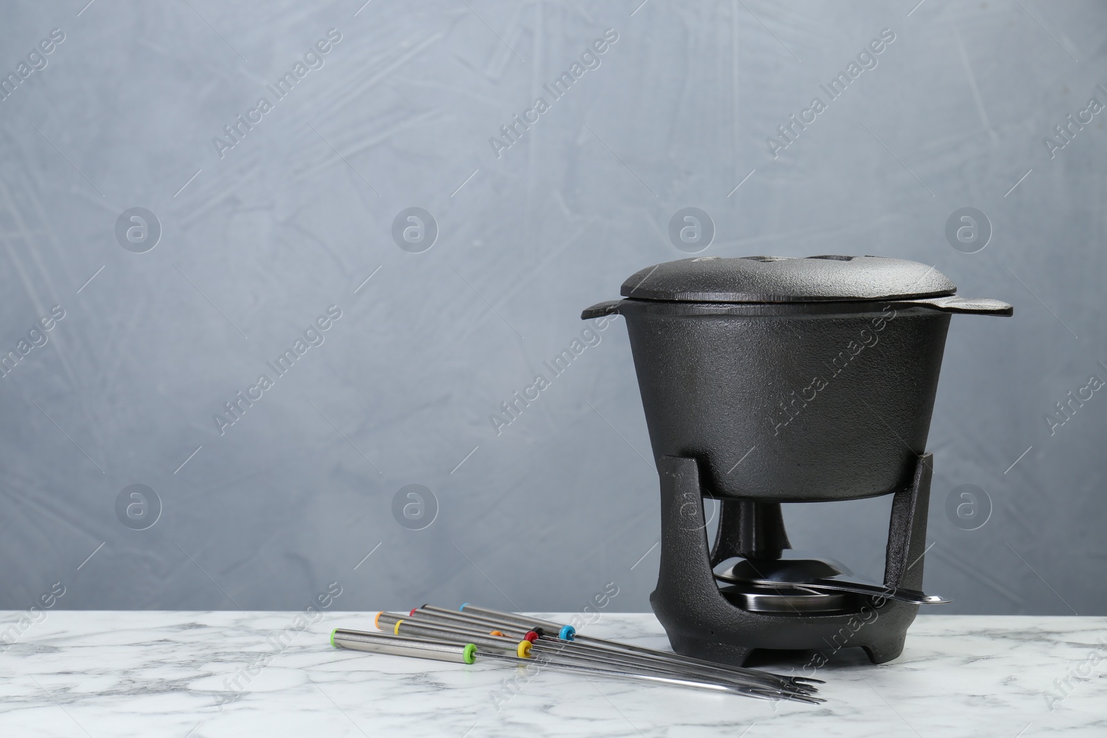 Photo of Fondue set on white marble table against light grey background, space for text