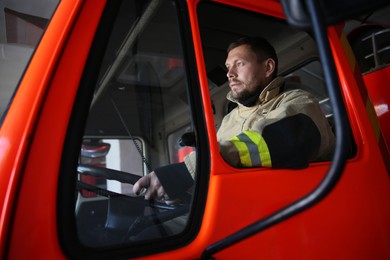 Photo of Firefighter in uniform driving modern fire truck