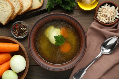Photo of Delicious chicken bouillon and ingredients on wooden table, flat lay