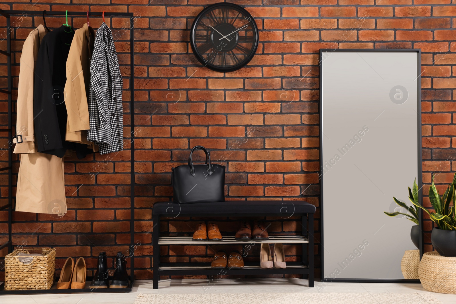 Photo of Stylish hallway with coat rack, mirror and shoe storage bench near brick wall. Interior design