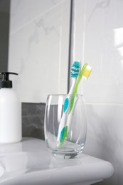 Photo of Light blue and green toothbrushes in glass holder on washbasin