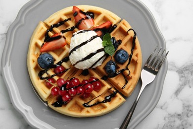 Photo of Delicious Belgian waffles with ice cream, berries and chocolate sauce on light marble table, top view