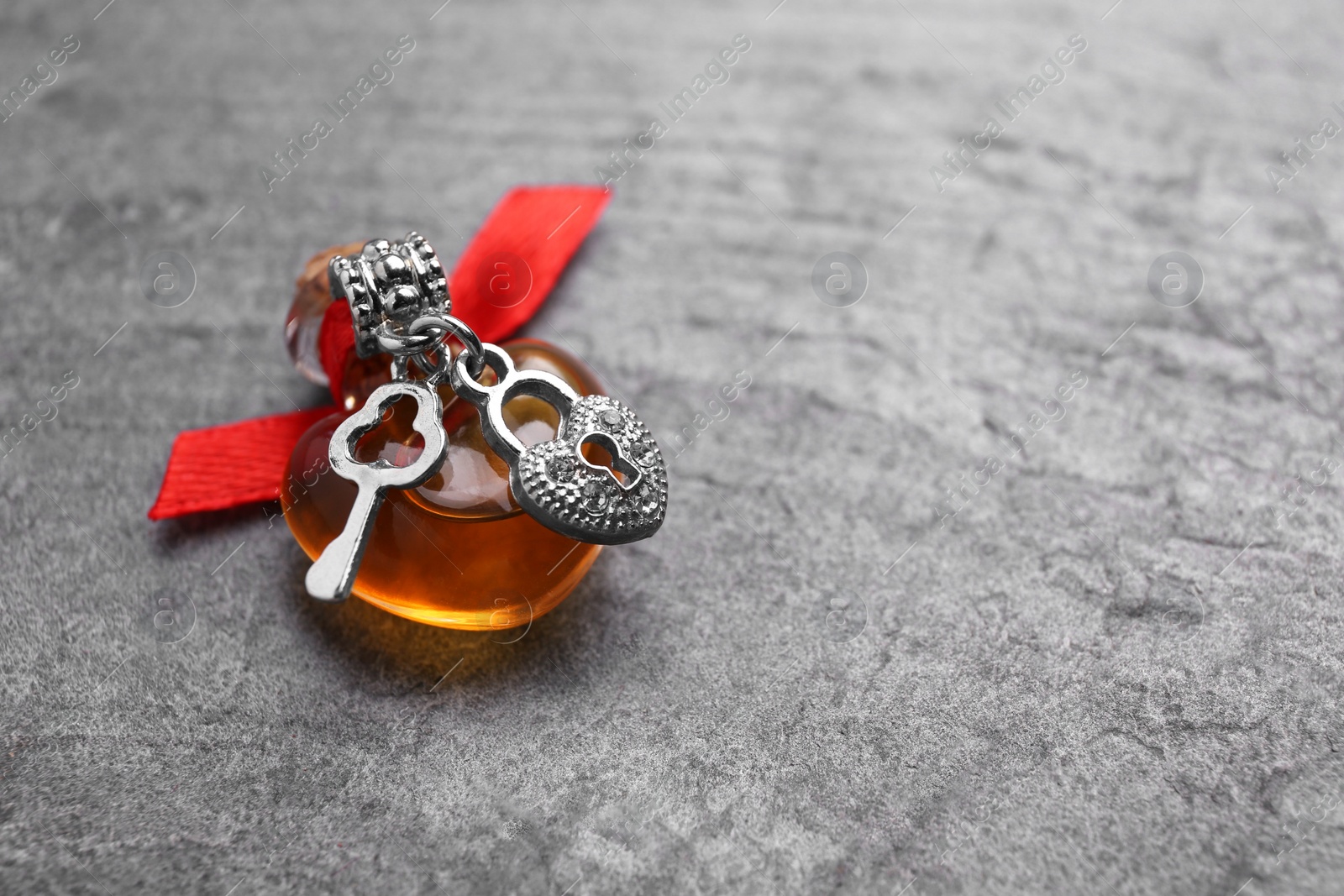 Photo of Heart shaped bottle of love potion with small key and padlock on grey table, space for text