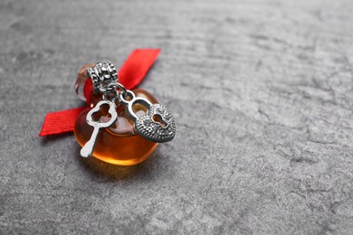 Photo of Heart shaped bottle of love potion with small key and padlock on grey table, space for text
