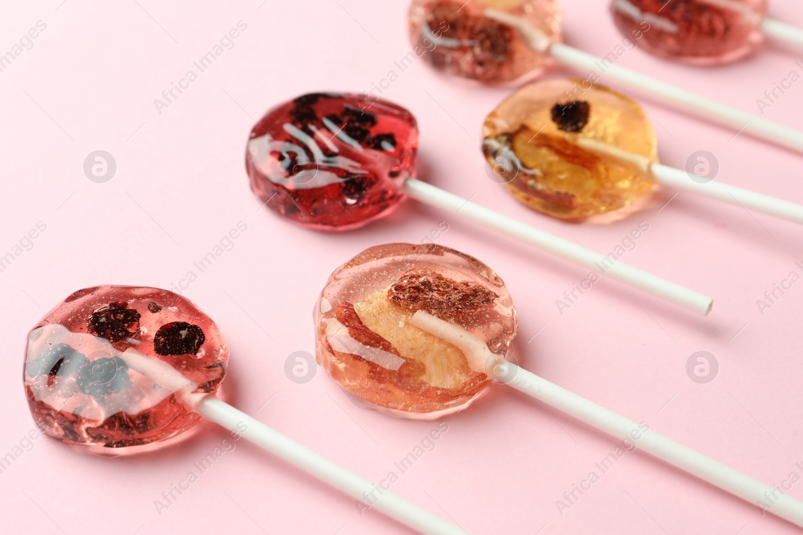 Photo of Sweet colorful lollipops with berries on pink background, closeup