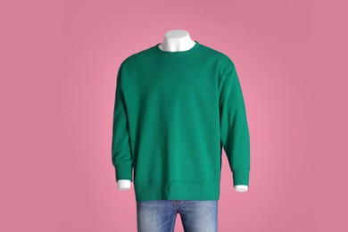Male mannequin dressed in stylish green sweatshirt and jeans on pink background