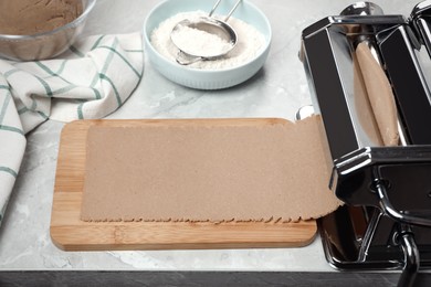 Preparing dough for soba (buckwheat noodles) with pasta maker at light grey table