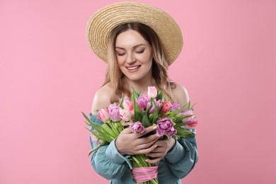 Photo of Happy young woman in straw hat holding bouquet of beautiful tulips on pink background