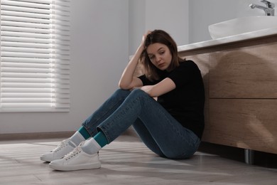 Photo of Sad young woman sitting on floor indoors