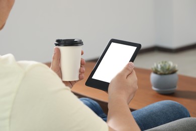 Photo of Man with cup of coffee using e-book reader indoors, closeup