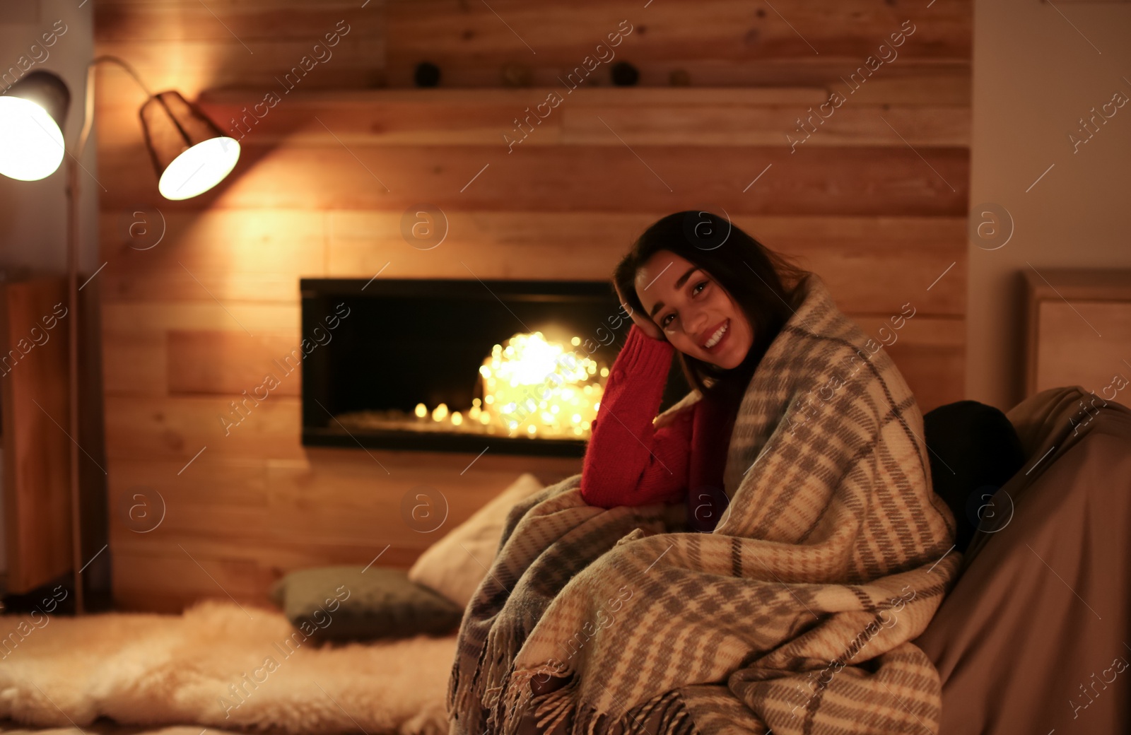 Photo of Young woman resting near decorative fireplace at home. Winter season