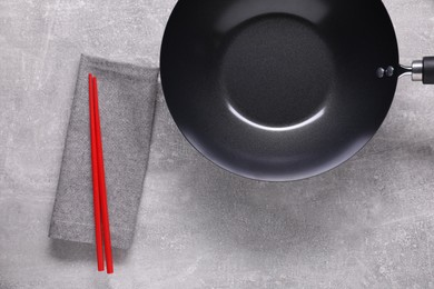 Empty iron wok and chopsticks on grey table, flat lay