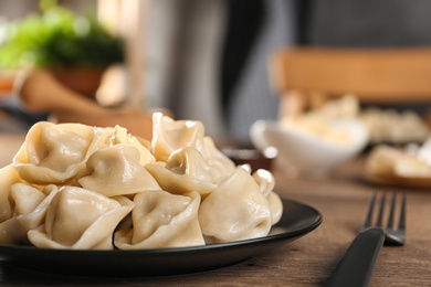 Photo of Tasty dumplings with butter on wooden table against blurred background