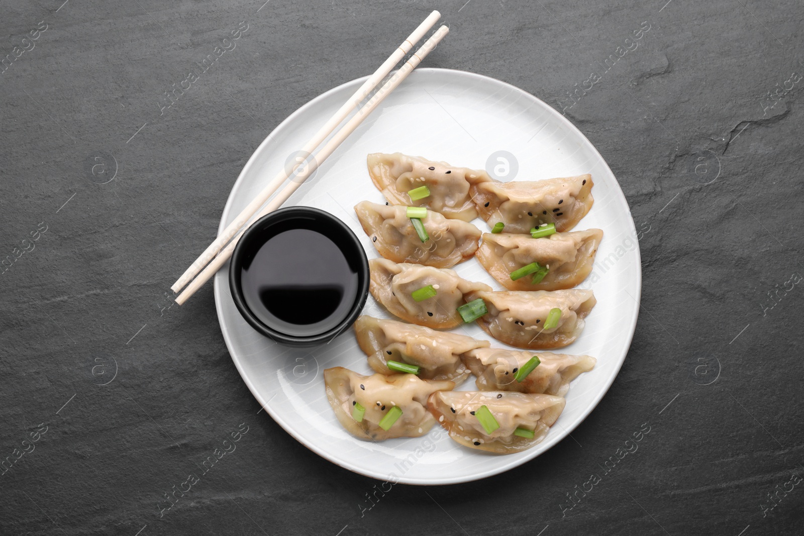 Photo of Delicious gyoza (asian dumplings) with green onions, soy sauce and chopsticks on gray table, top view