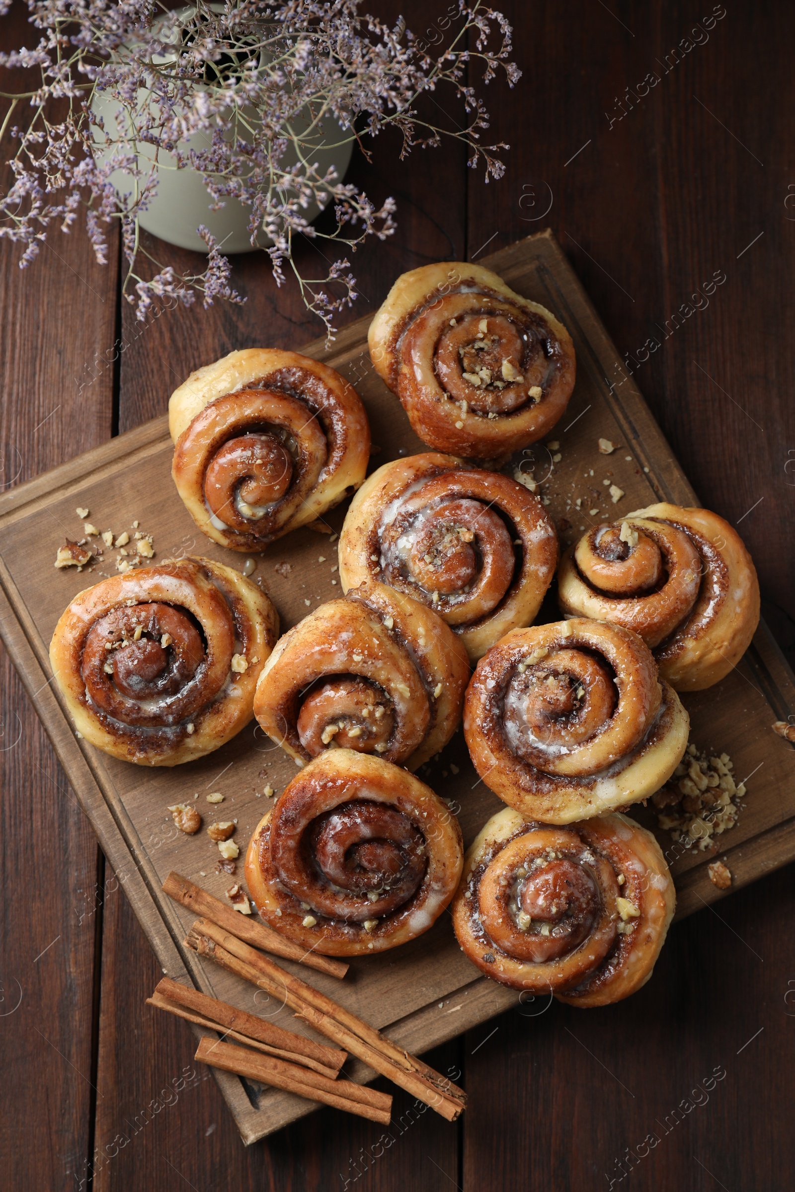 Photo of Tasty cinnamon rolls, sticks and nuts on wooden table, top view