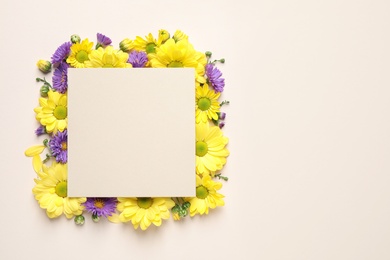 Beautiful chamomile flowers and paper card on beige background, flat lay with space for text