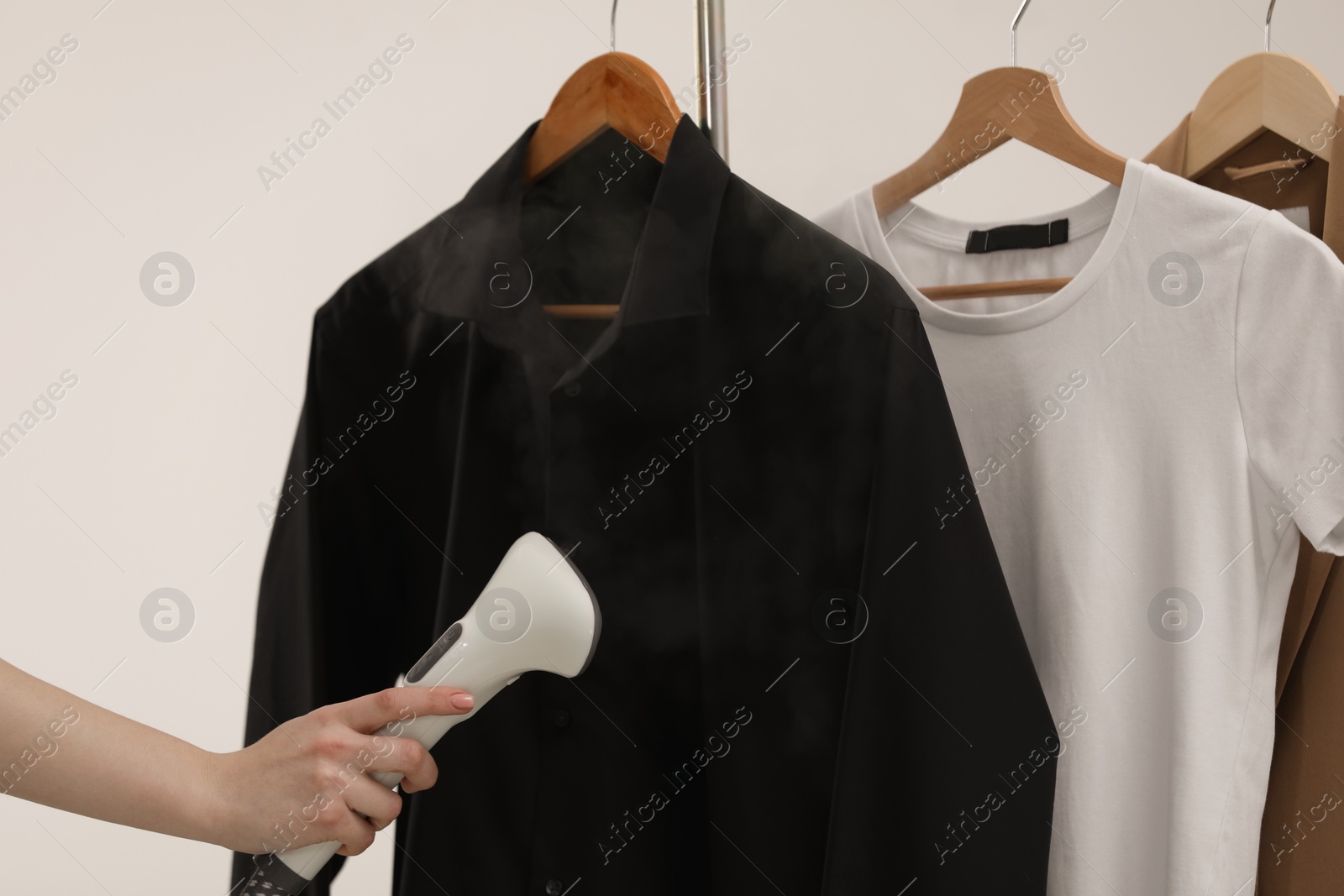 Photo of Woman steaming black shirt on white background, closeup