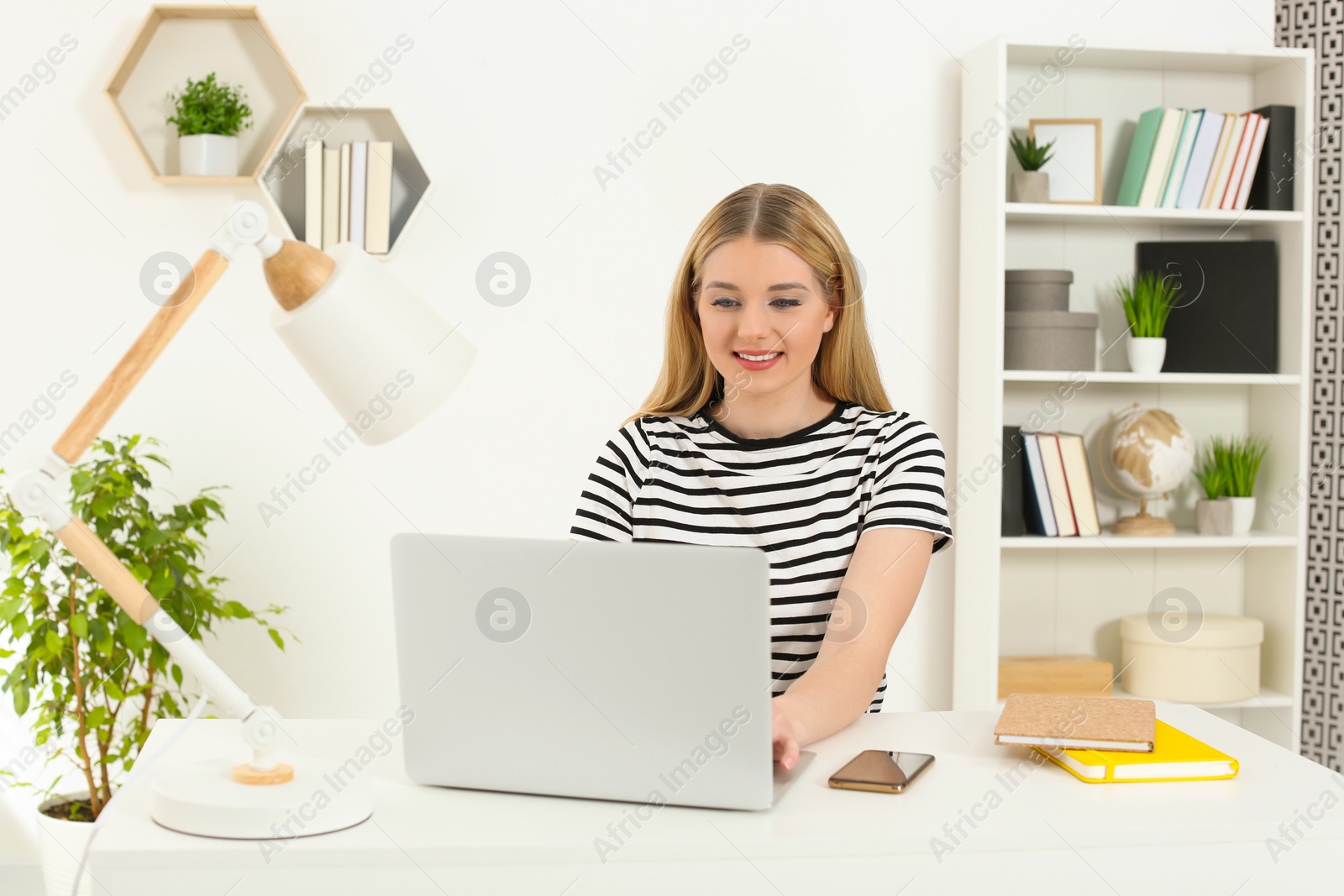 Photo of Home workplace. Woman working on laptop at white desk in room