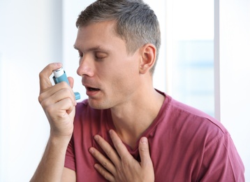 Photo of Young man using asthma inhaler at home