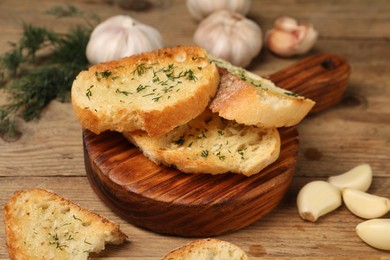 Tasty baguette with garlic and dill on wooden table