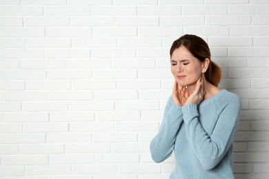 Woman suffering from cough near brick wall. Space for text