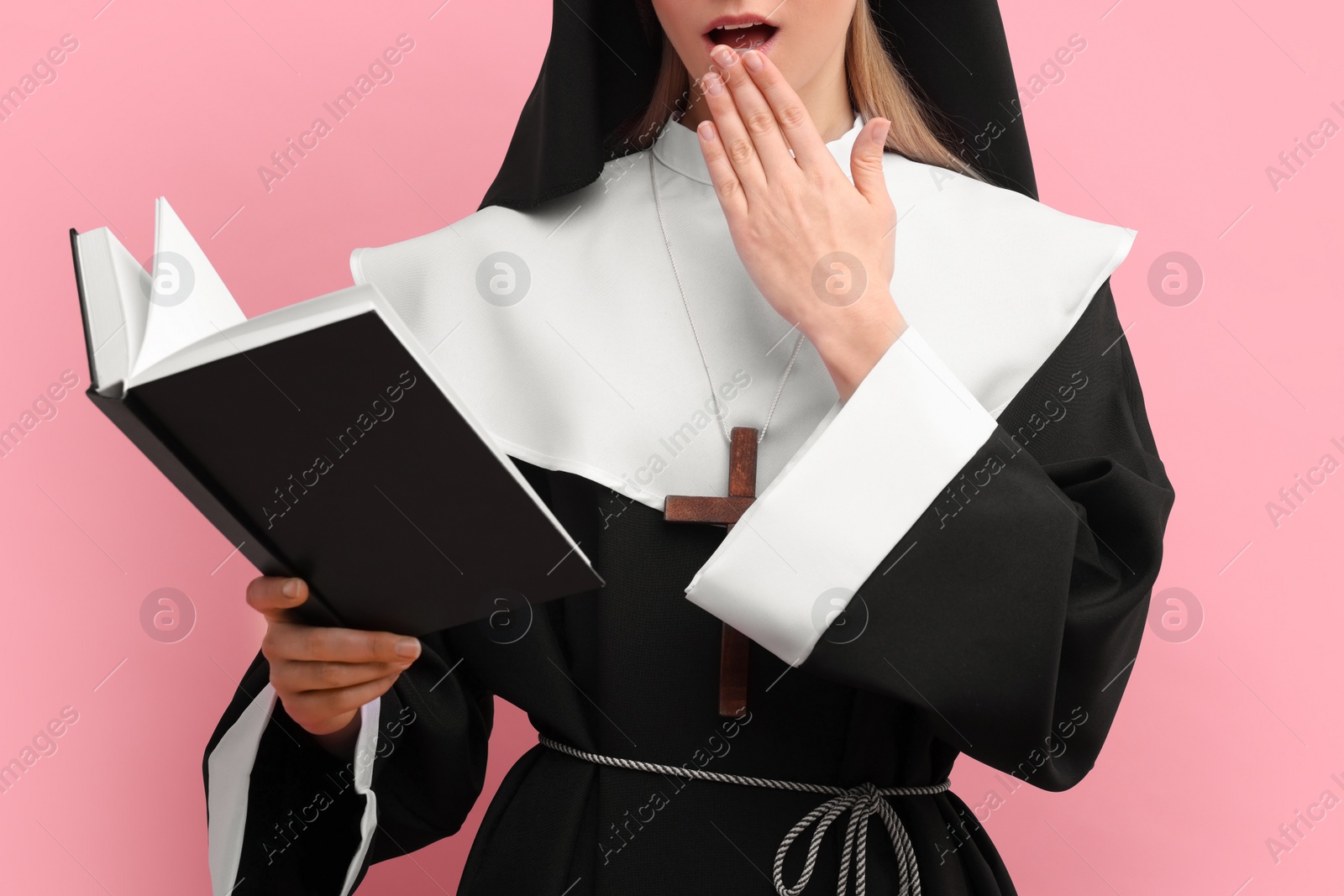 Photo of Surprised woman in nun habit reading Bible against pink background, closeup