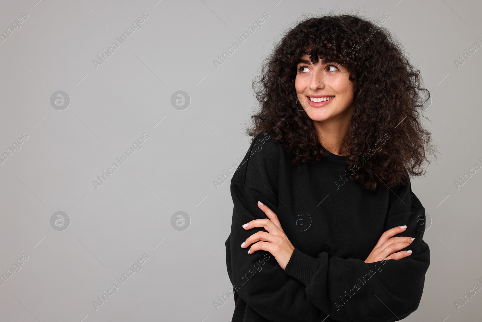 Photo of Happy young woman in stylish black sweater on light grey background, space for text