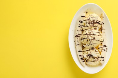Photo of Delicious banana split ice cream with toppings on yellow background, top view. Space for text