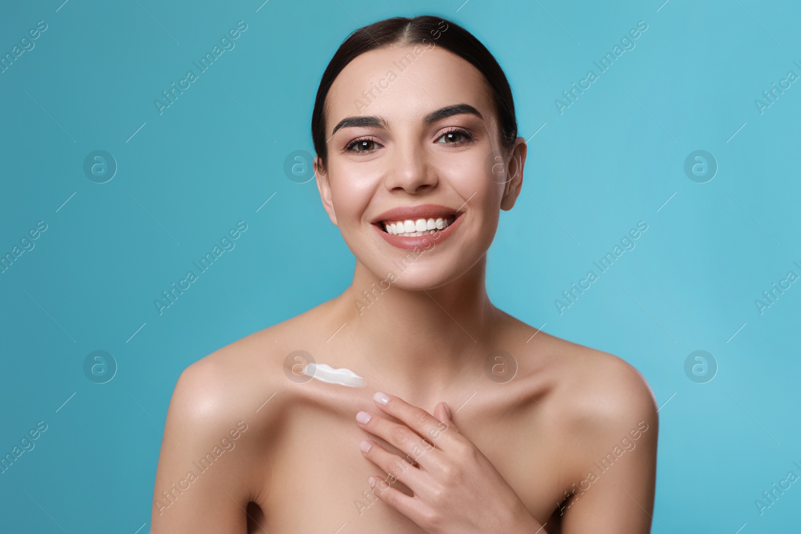 Photo of Young woman applying body cream onto her neck against turquoise background