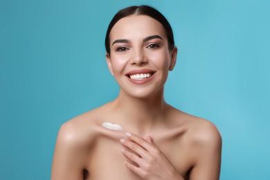 Young woman applying body cream onto her neck against turquoise background