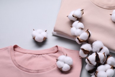 Photo of Cotton branch with fluffy flowers and t-shirts on light gray background, above view