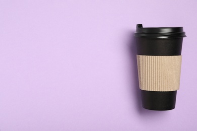 Photo of Takeaway paper coffee cup with cardboard sleeve on violet background, top view. Space for text