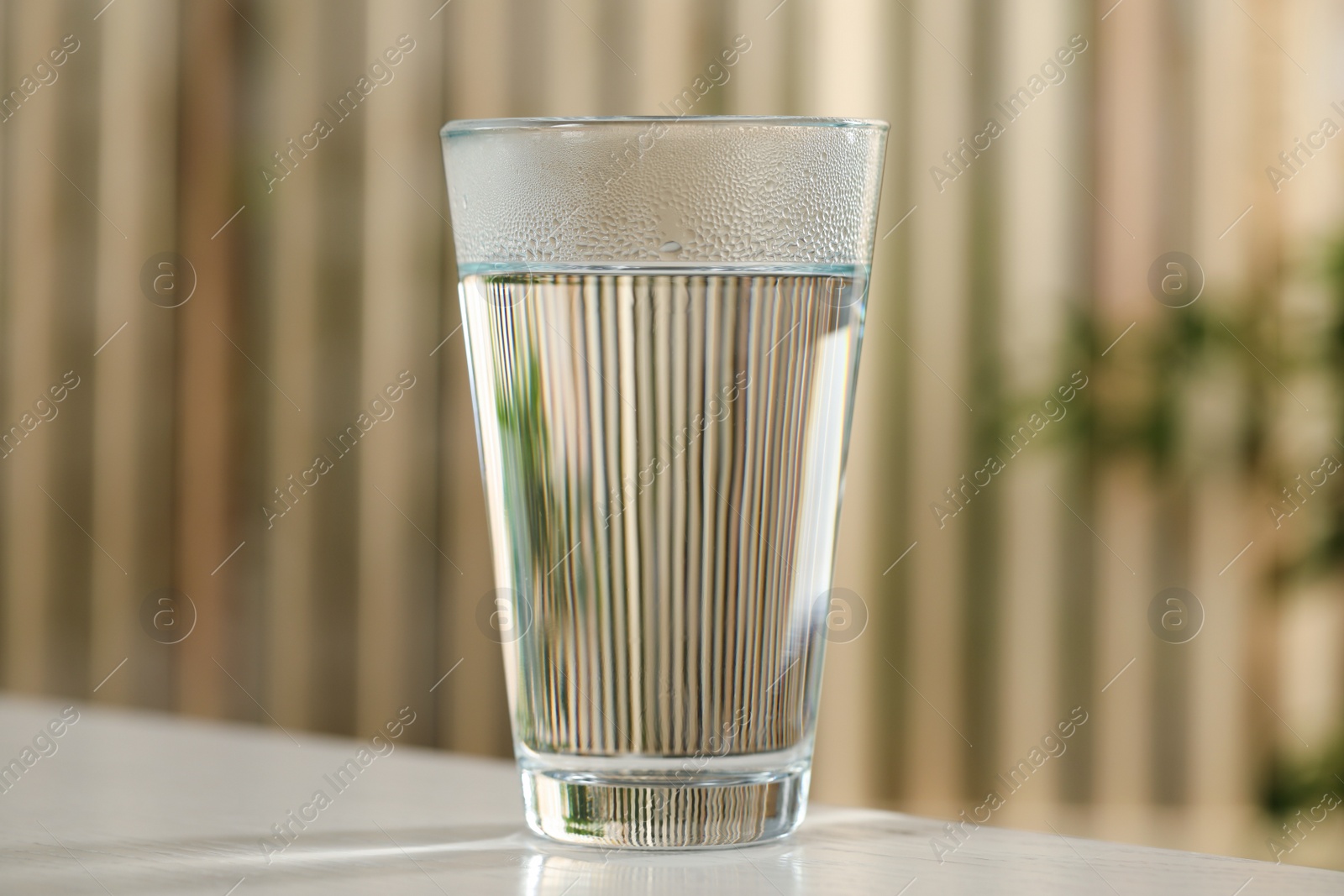 Photo of Glass of pure water on white table against blurred background